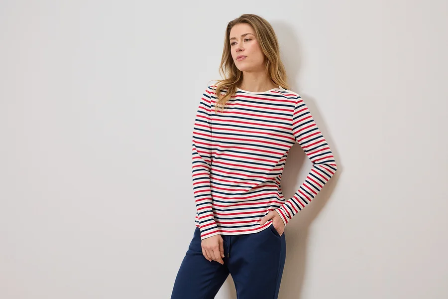 Frau mit gestreiftem Langarmshirt und blauer Jogginghose, eine Hand in der Hosentasche.