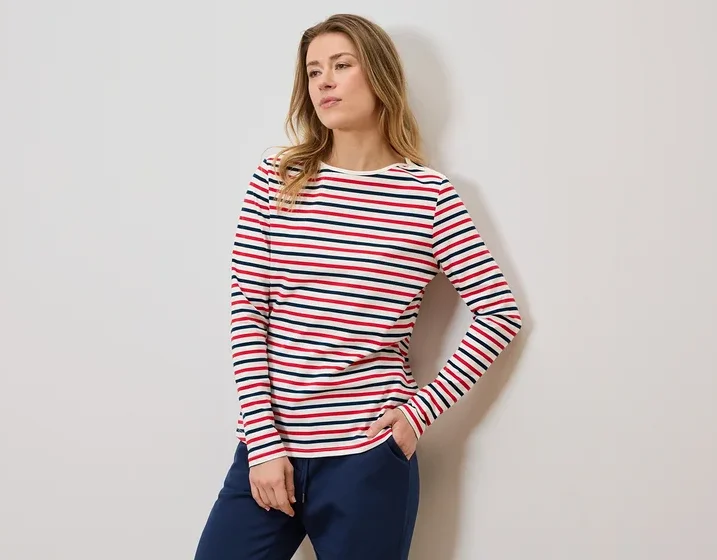 Frau mit gestreiftem Langarmshirt und blauer Jogginghose, eine Hand in der Hosentasche.