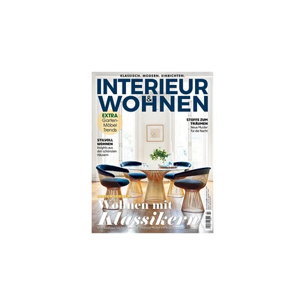 Magazincover für 'INTERIEUR & WOHNEN' zeigt ein modernes Esszimmer mit rundem Glastisch und vier Stühlen mit blauen Polstern und goldenen, skulpturalen Füßen. Im Hintergrund sind große Fenster sichtbar. Der Titel 'Wohnen mit Klassikern' ist aufgedruckt.