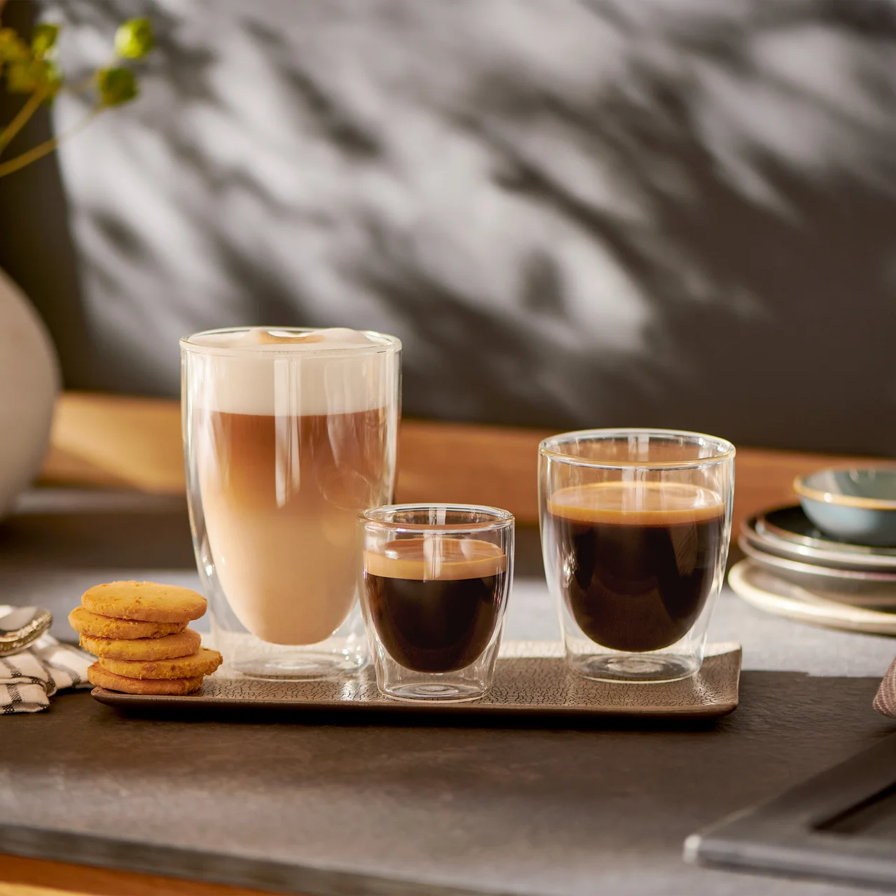 Drei Gläser mit Kaffee stehen nebeneinander auf einem Tablett. Links ein Cappuccino, in der Mitte ein Espresso und rechts ein Kaffee.