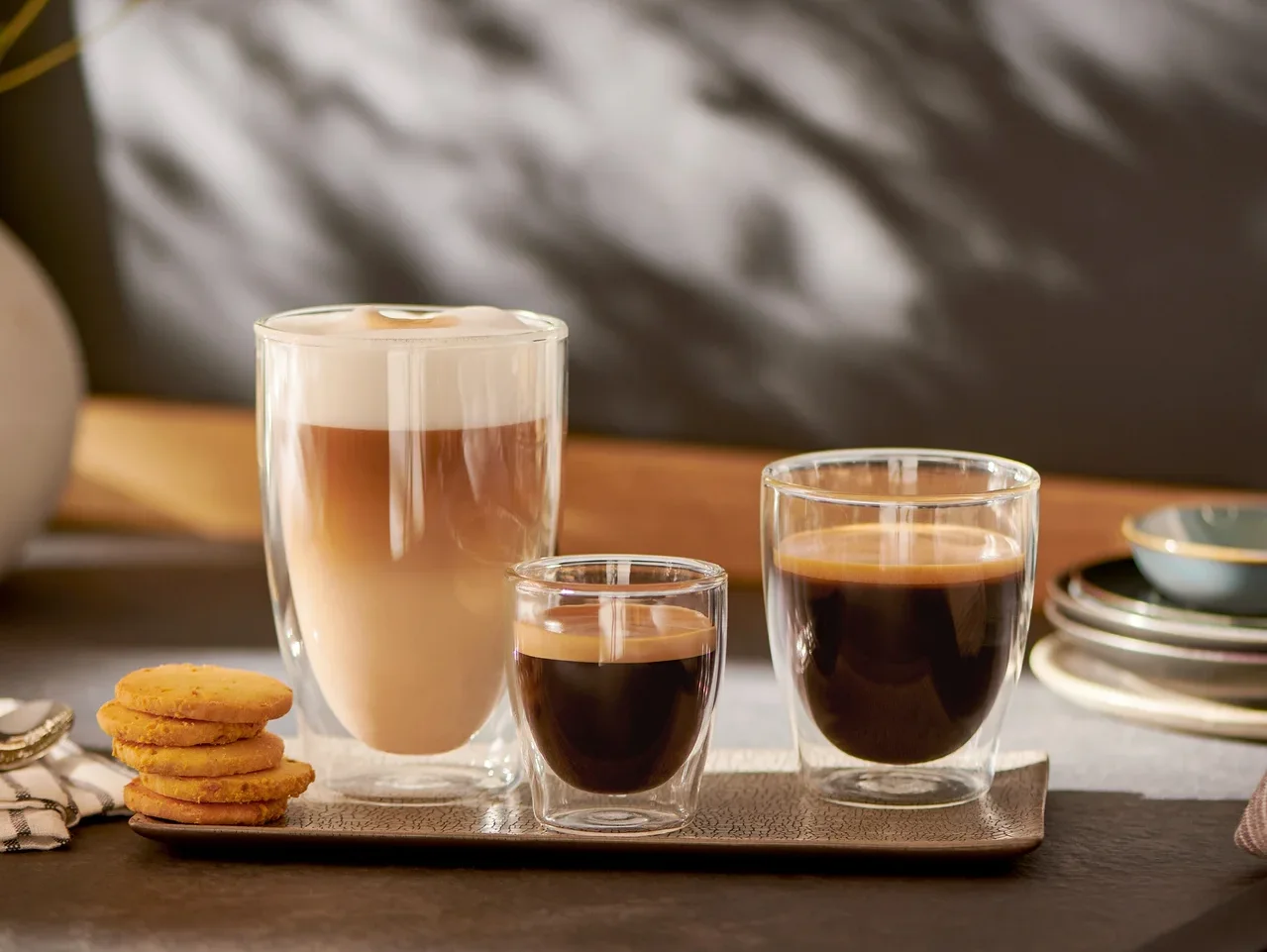 Drei Gläser mit Kaffee stehen nebeneinander auf einem Tablett. Links ein Cappuccino, in der Mitte ein Espresso und rechts ein Kaffee.