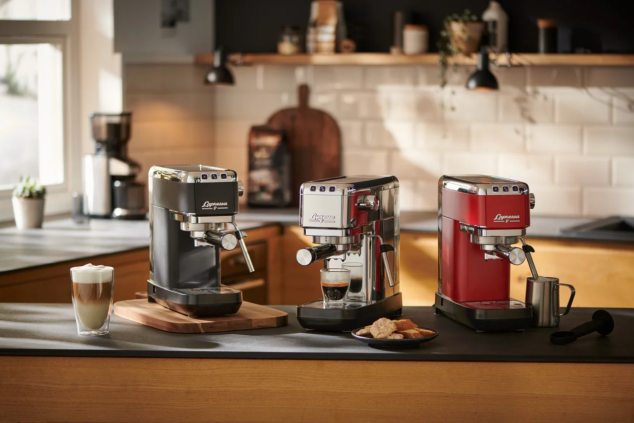Drei »Lapressa« Siebträgermaschinen (schwarz, silber und rot) stehen auf einer Küchentheke. Die silberne Maschine bereitet Espresso zu.