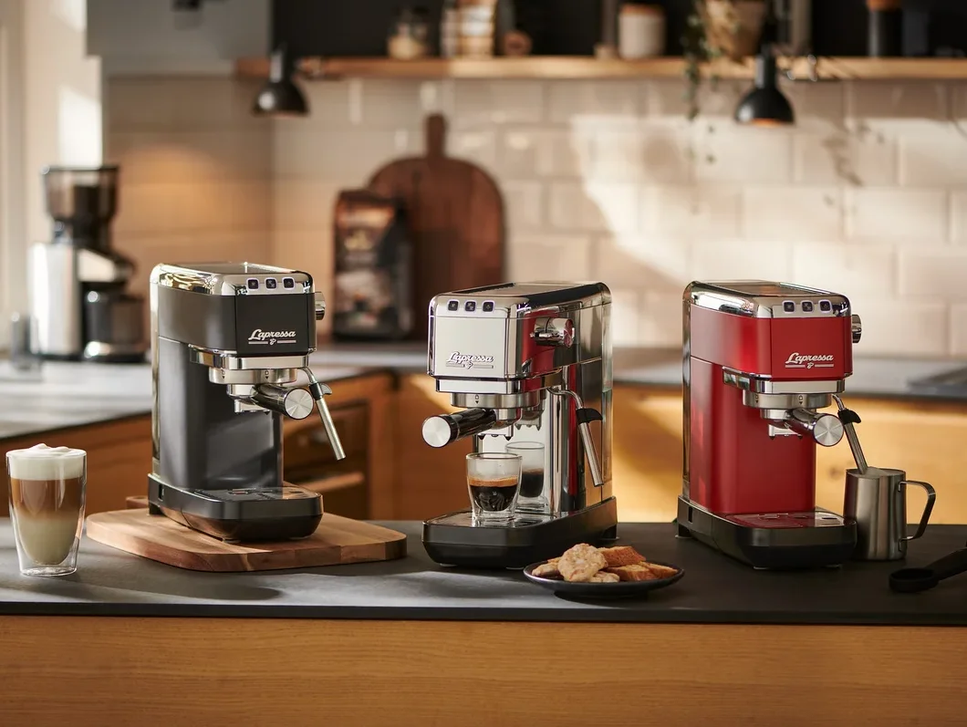 Drei »Lapressa« Siebträgermaschinen (schwarz, silber und rot) stehen auf einer Küchentheke. Die silberne Maschine bereitet Espresso zu.