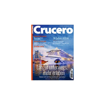 Magazincover „Crucero“ mit dem nachts beleuchteten Kreuzfahrtschiff „AIDAperla“ mit Kussmund-Logo im Hafen vor einer Stadtkulisse. Titel: „Länger unterwegs, mehr erleben“.