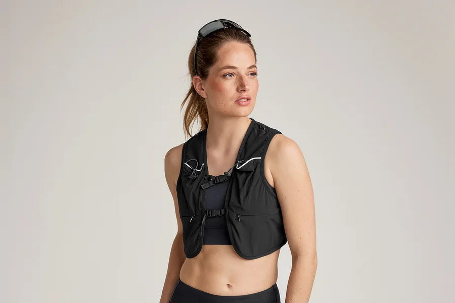 Frau mit Sonnenbrille auf dem Kopf trägt eine schwarze Laufweste über einem Sport-BH und Leggings.