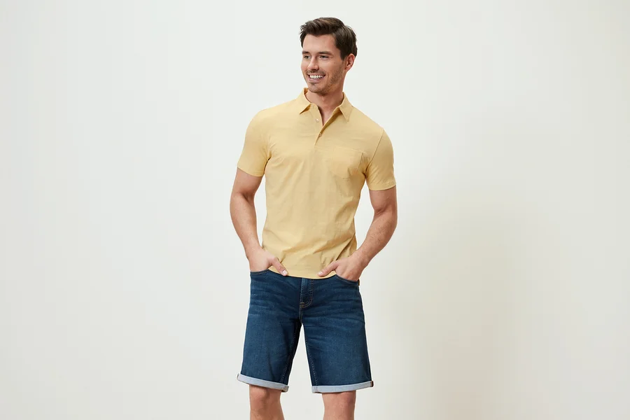 Mann posiert in gelb meliertem Jersey-Poloshirt und Jeansshorts.