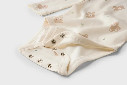 Nahaufnahme eines hellen Baby-Bodys mit Bären- und Herzmuster und Druckknöpfen im Schritt.