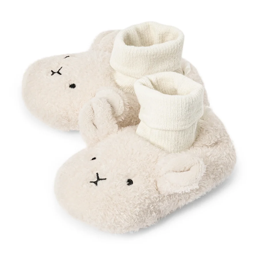 Nahaufnahme von zwei flaumigen, cremefarbenen Baby-Hausschuhen mit Hasengesicht und weißen Socken