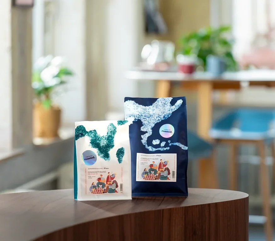 Zwei Kaffeepackungen stehen auf einem Tisch, eine weiße und eine blaue.