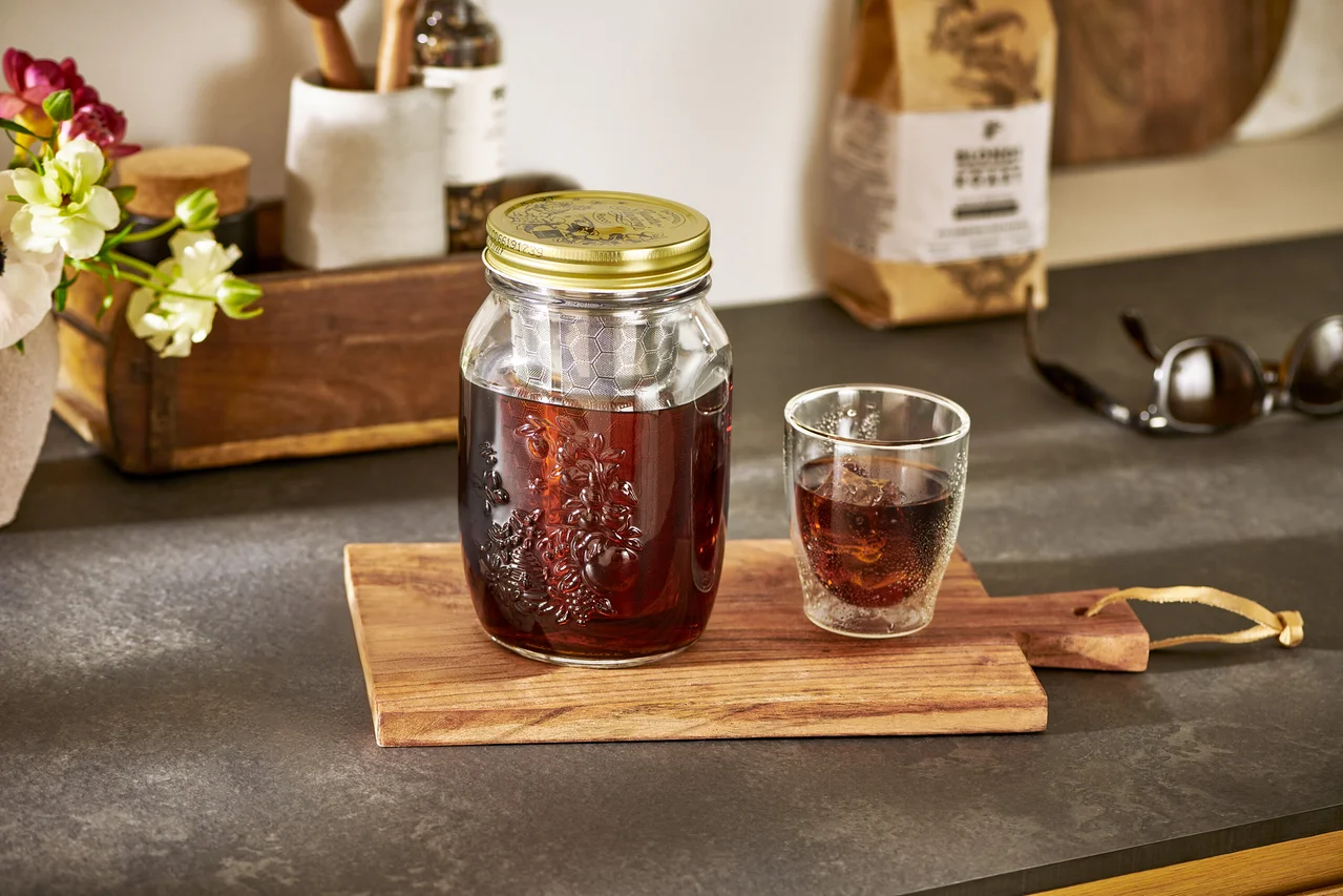 Kalter Kaffee im Cold Brew Maker »BrewJar« steht neben einem Glas auf einem Holzbrett.