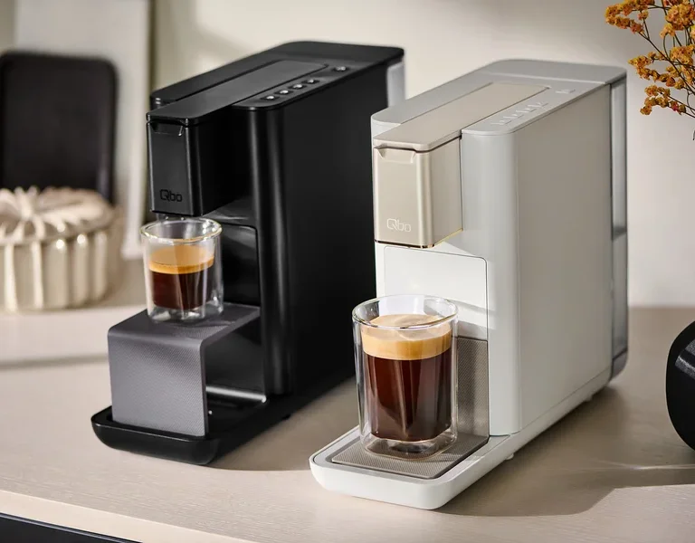 Zwei Qbo Kaffeemaschinen stehen nebeneinander und bereiten Kaffee in Gläsern zu.