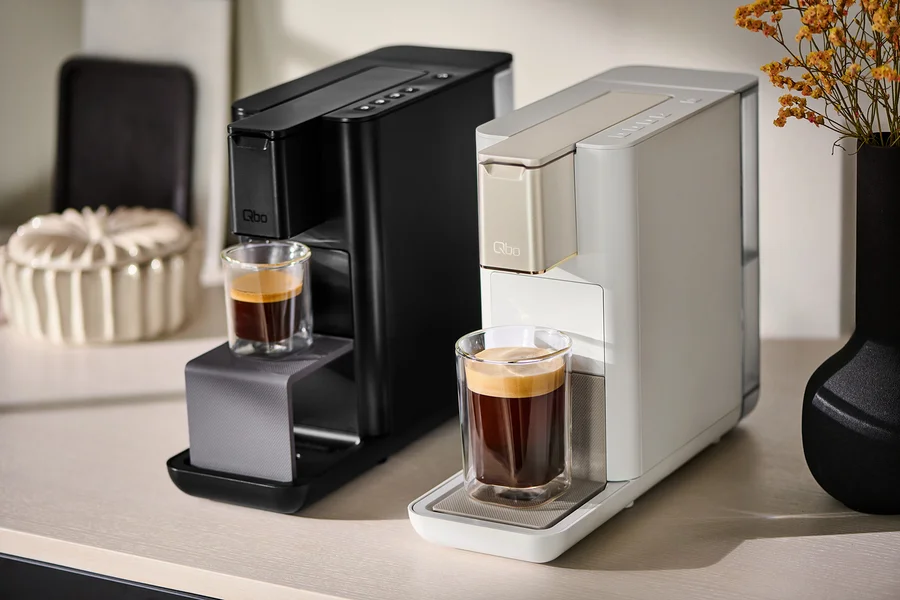 Zwei Qbo Kaffeemaschinen stehen nebeneinander und bereiten Kaffee in Gläsern zu.