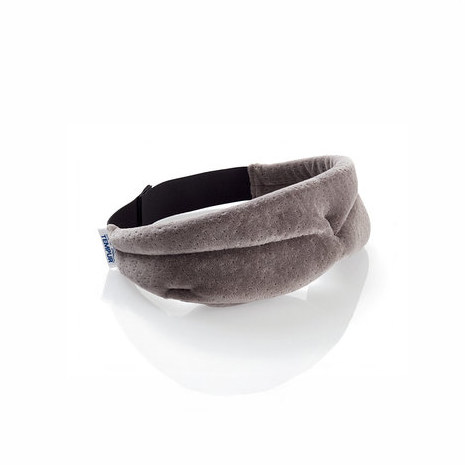 Eine graue, konturierte Schlafmaske mit einem schwarzen Gummiband und einem kleinen weißen „TEMPUR“-Etikett, auf einer weißen Oberfläche mit Reflexion liegend.
