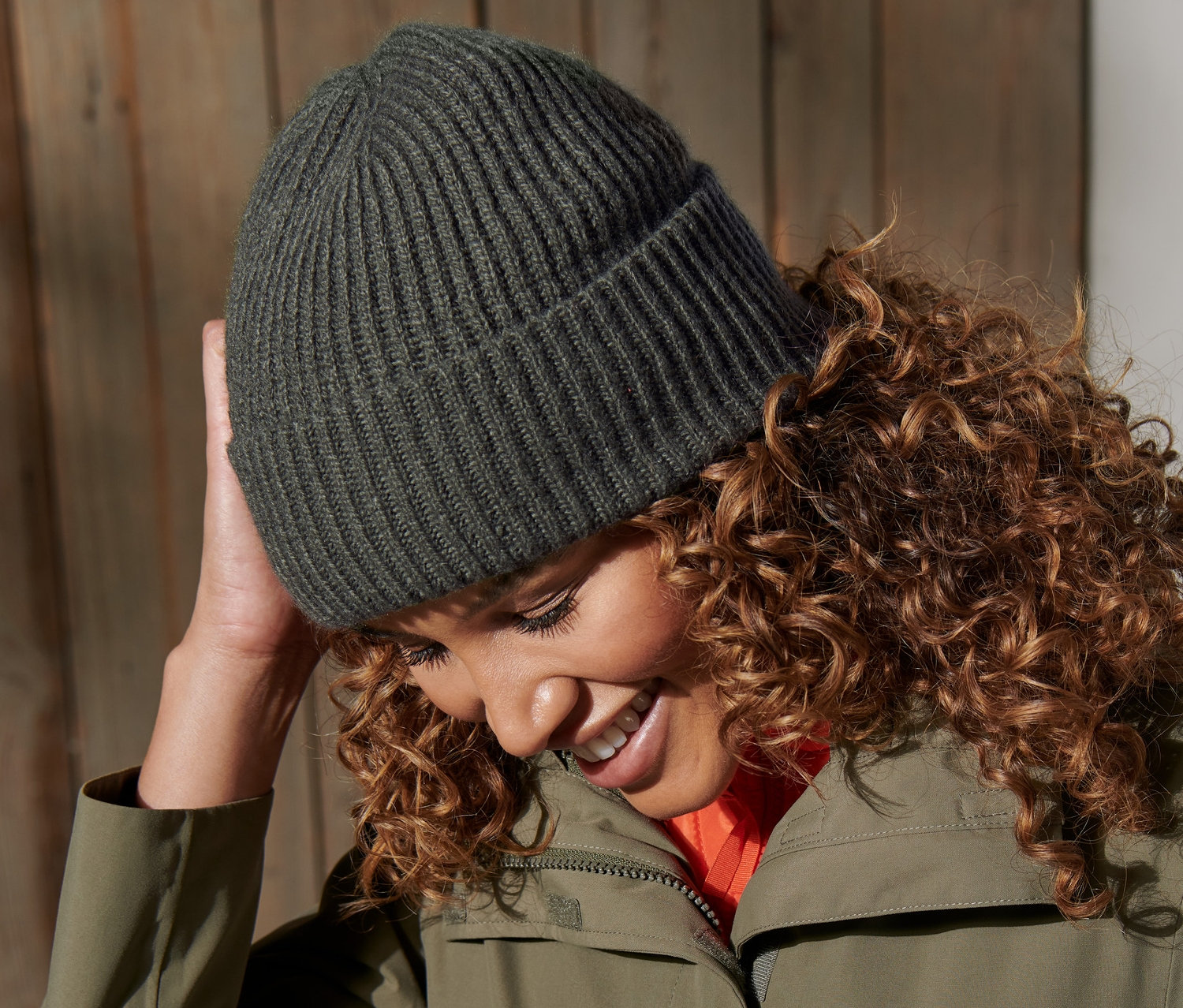 Frau lächelt und berührt eine grüne Strickmütze.