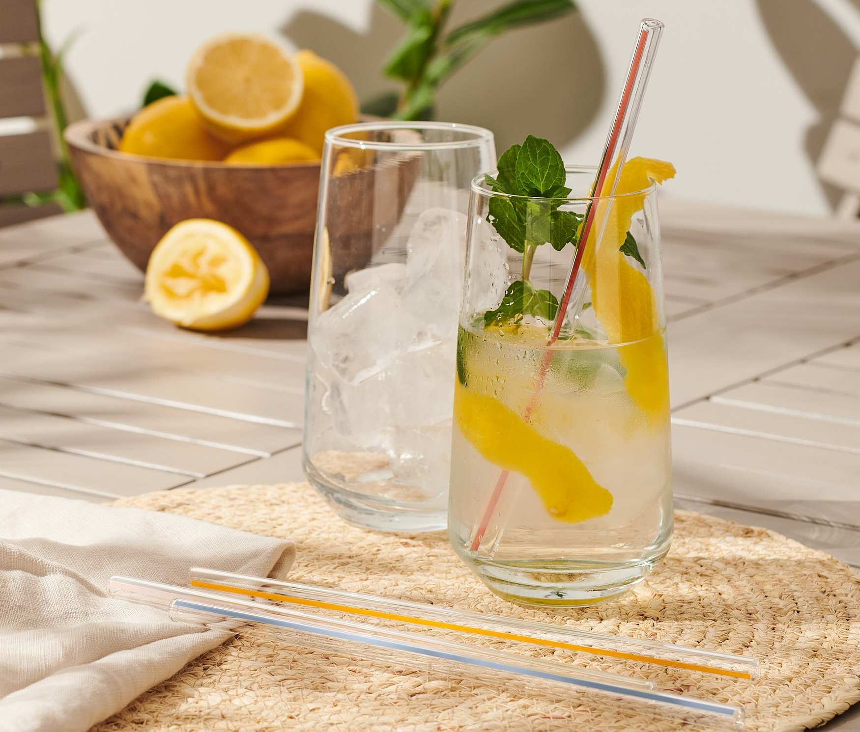 Zwei Getränke mit Zitrone und Minze auf einem Tisch, daneben eine Holzschüssel mit Zitronen und 4 Glas-Trinkhalme.