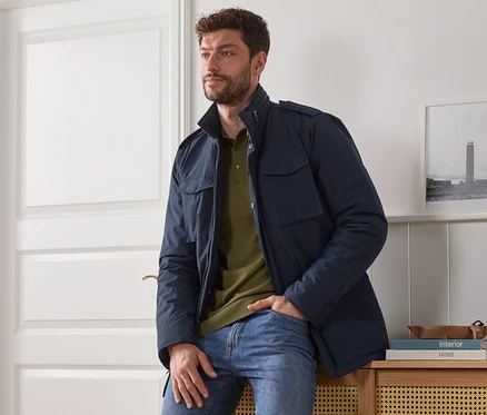 Mann sitzt auf Schrank, trägt blaue Fieldjacket.