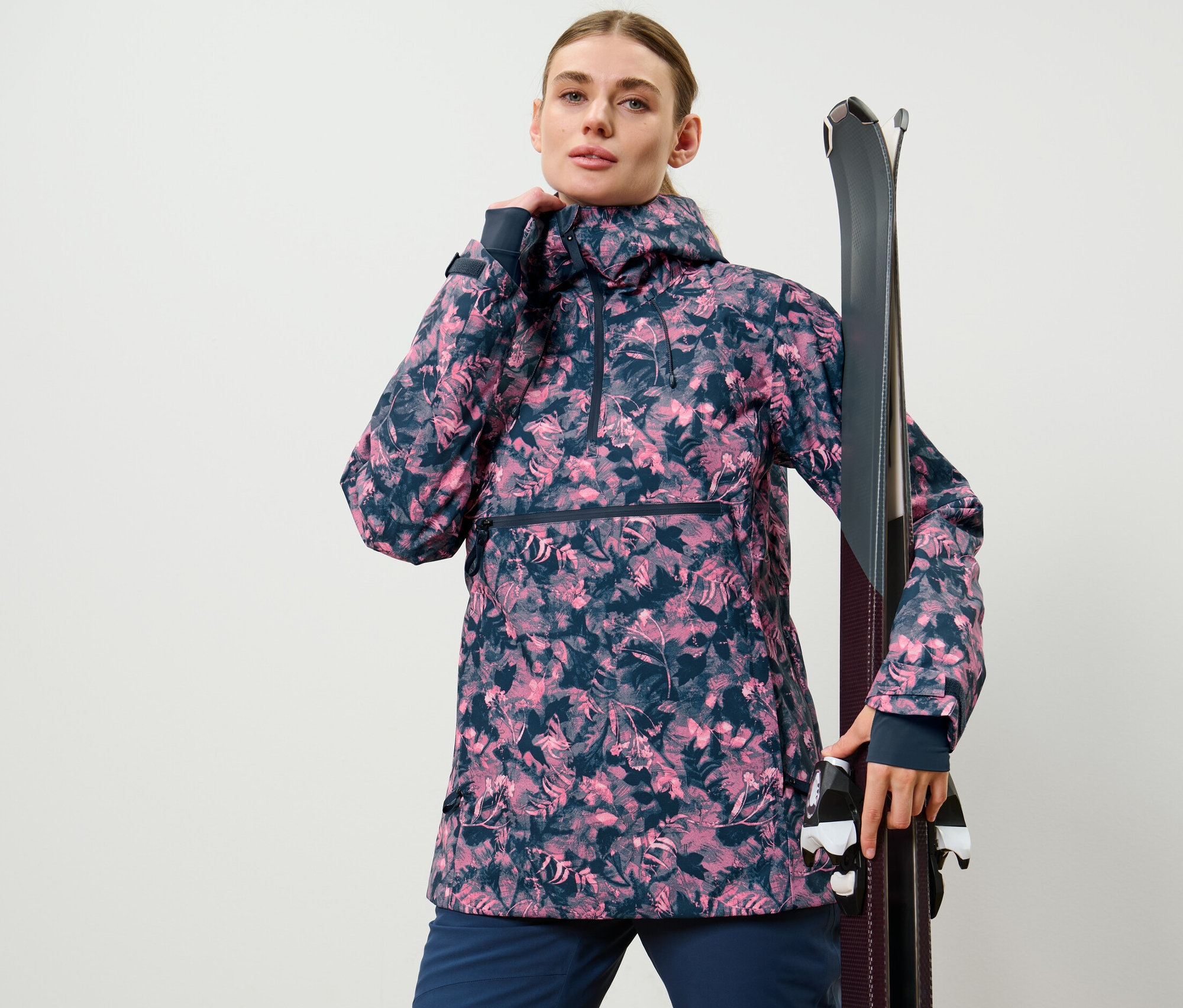 Frau posiert in Halfzip-Skijacke mit Alloverprint und hält Ski.