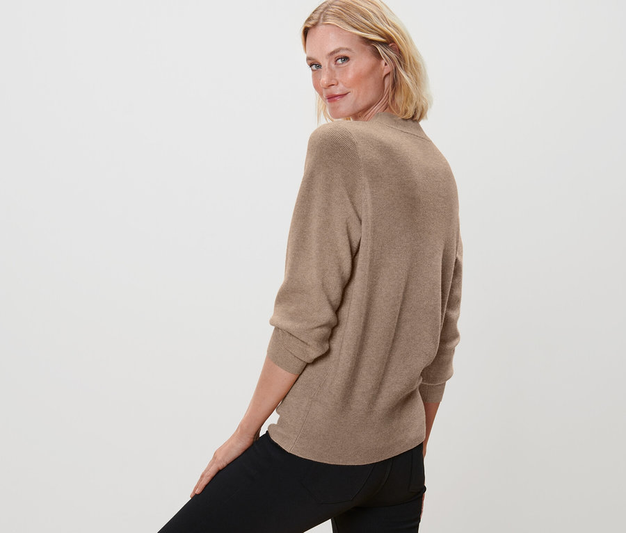 Frau blickt über die Schulter und posiert in Feinstrickpullover, beige meliert und schwarzen Jeans.