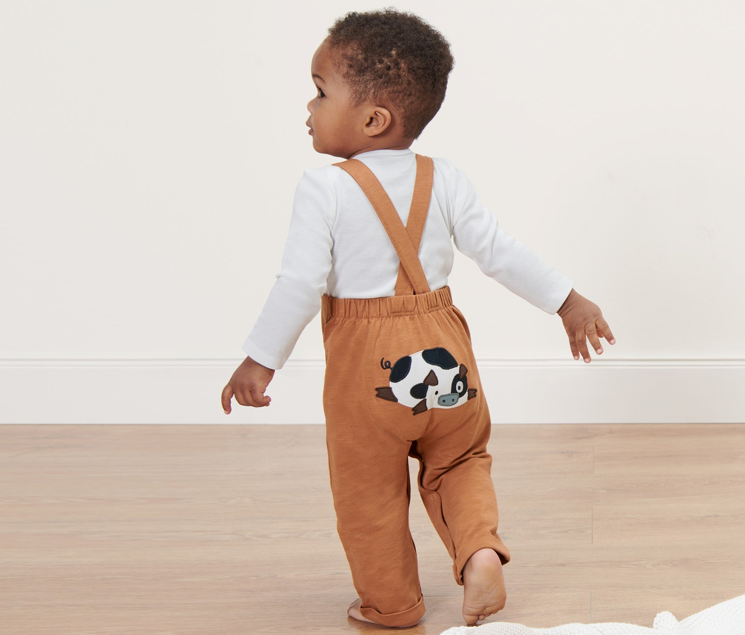 Kleinkind trägt eine Baby-Latzhose mit einem liegenden Kuh-Patch.