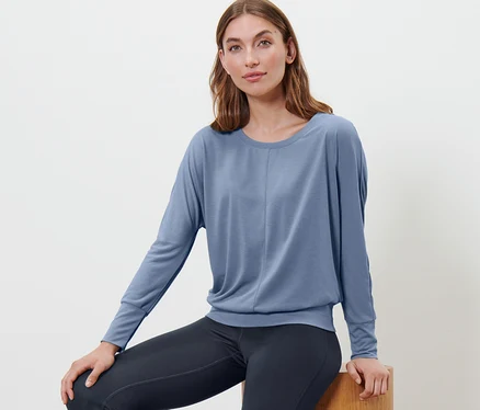 Frau sitzt auf einem Holzhocker und trägt ein blaues Sport-und-Yogashirt.