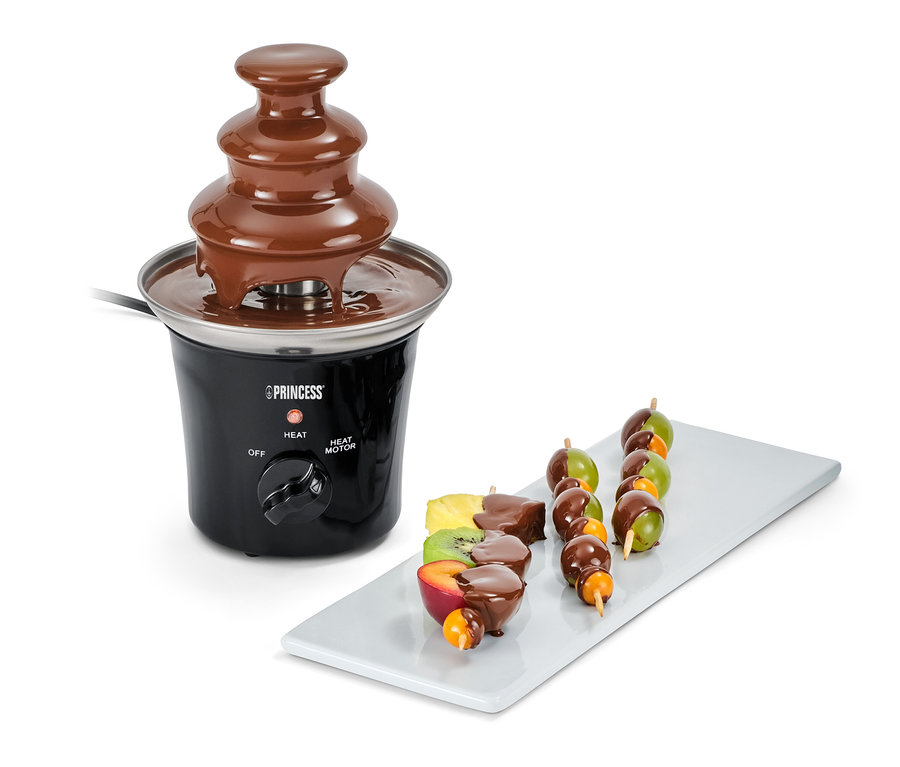 Elektrischer Mini-Schokobrunnen mit Fruchtspießen auf einem weißen Teller.