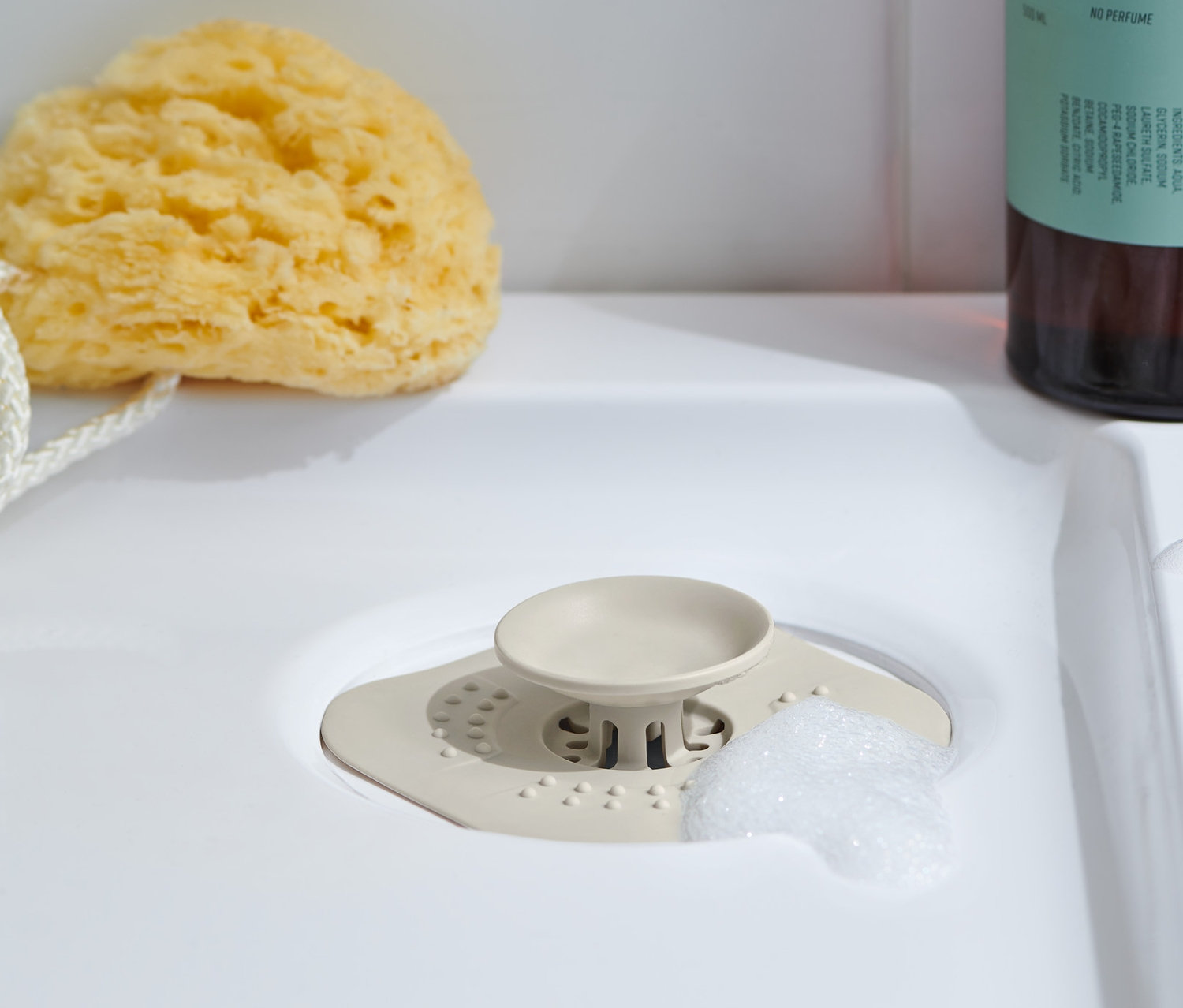 Abflusssieb/-verschluss liegt im Waschbecken, daneben ein Badeschwamm und dahinter eine Flasche Duschgel.