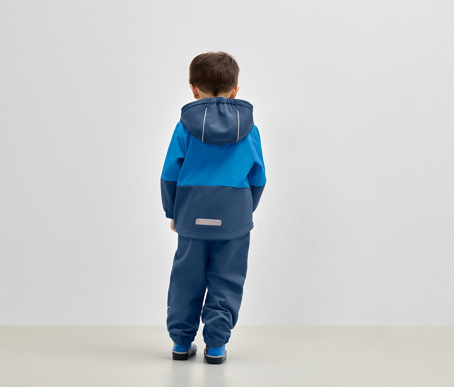 Ein Junge steht mit dem Rücken zum Betrachter und trägt eine blaue Kapuzenjacke und blaue Hosen.