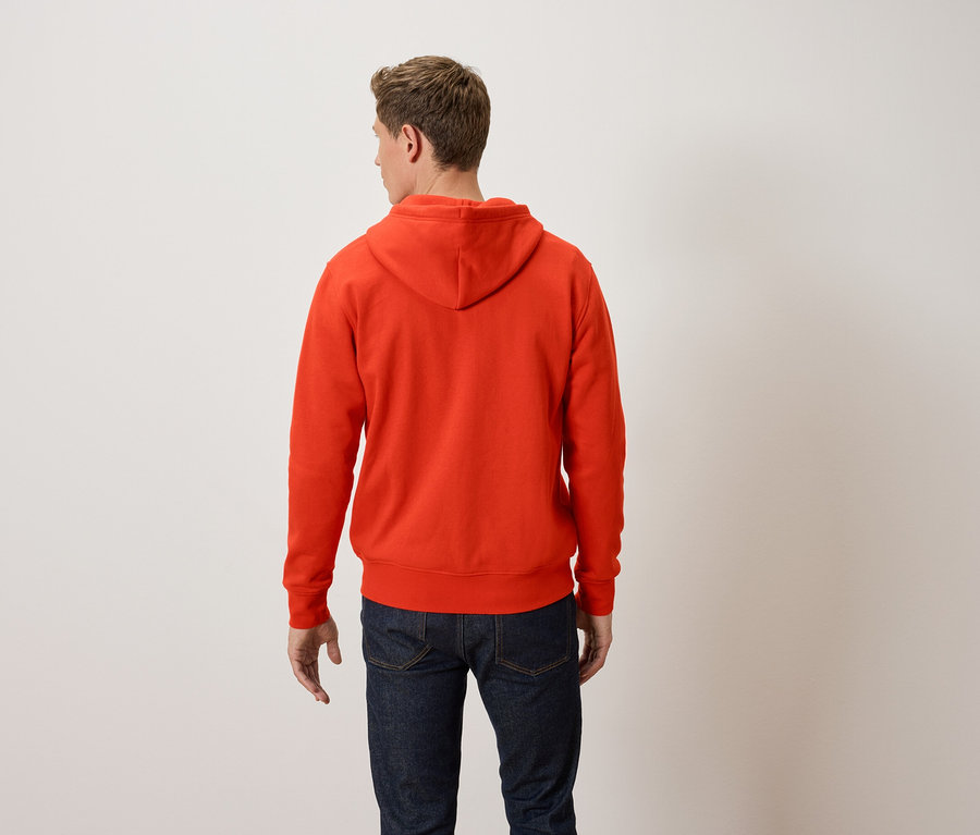 Ein Mann mit dem Rücken zur Kamera trägt einen orangefarbenen Kapuzenpullover und blaue Jeans.