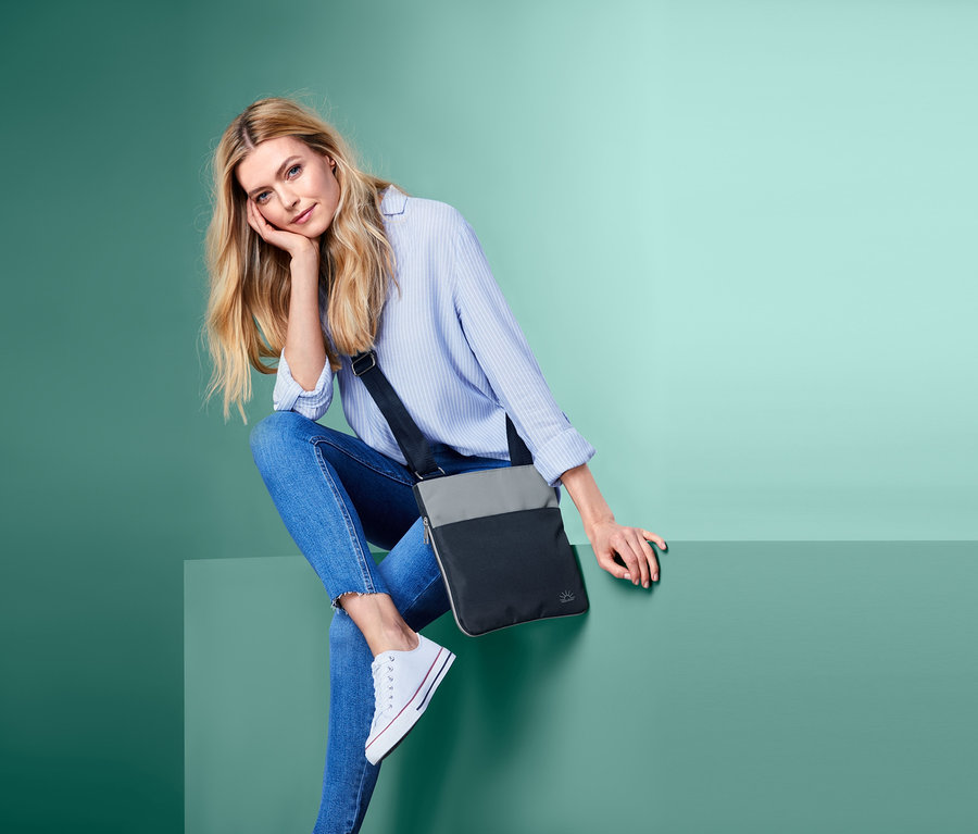 Blonde Frau sitzt und posiert mit einer blau-grauen Sicherheits-Umhängetasche.