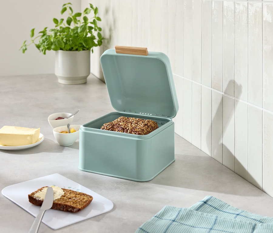 Offene hellblaue Brotdose mit Brot, daneben Butter, Marmelade, Messer und bestrichenes Brot.