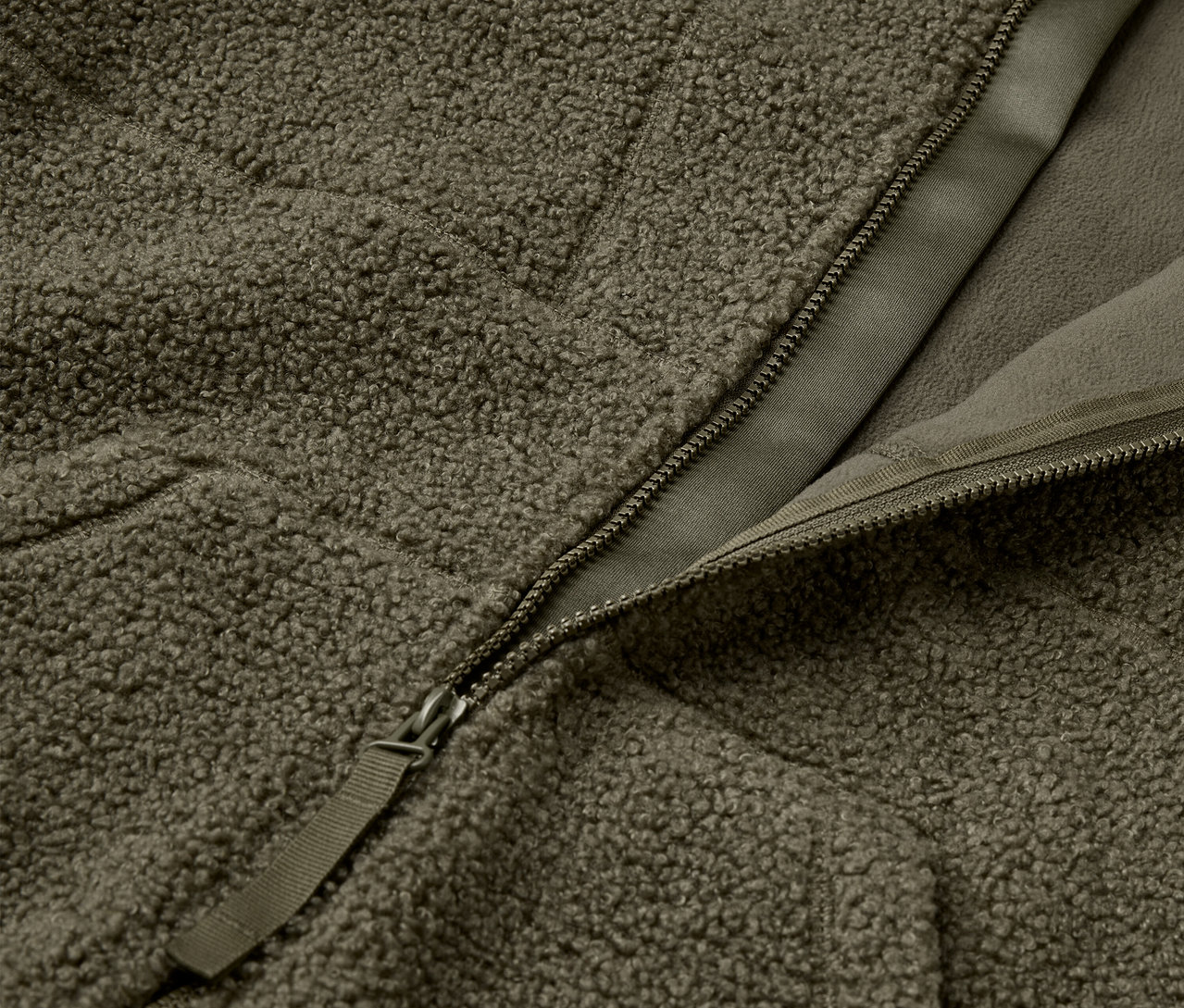 Detailaufnahme einer olivgrünen, flauschigen Jacke mit Reißverschluss.