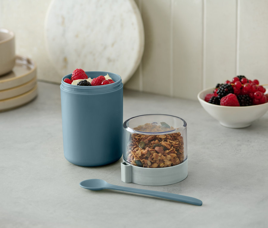 Ein grüner To-go-Joghurt-Becher mit Müsli und Beeren.