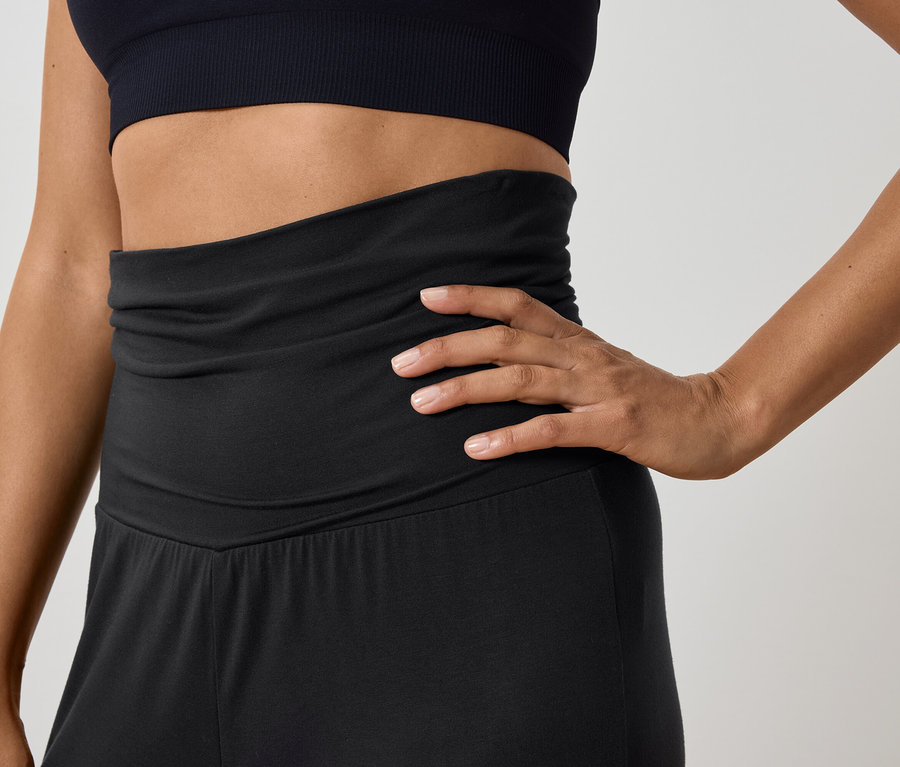 Frau posiert in schwarzem Sportoberteil und hoch taillierter Hose.