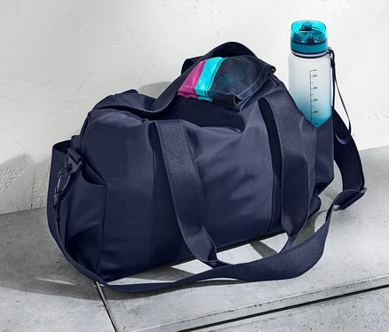 Eine dunkelblaue Sporttasche und eine Wasserflasche auf einer Betonoberfläche.
