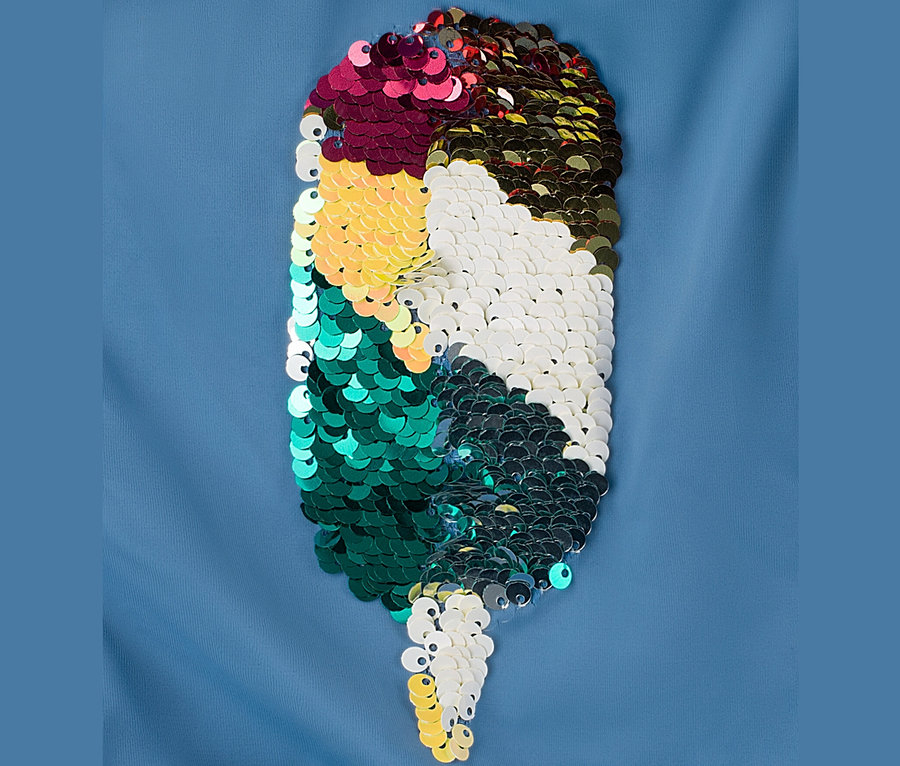 Detailaufnahme eines Kinder-Badeanzugs mit Wendepailletten in Tropfenform, angeordnet in Farbblöcken.