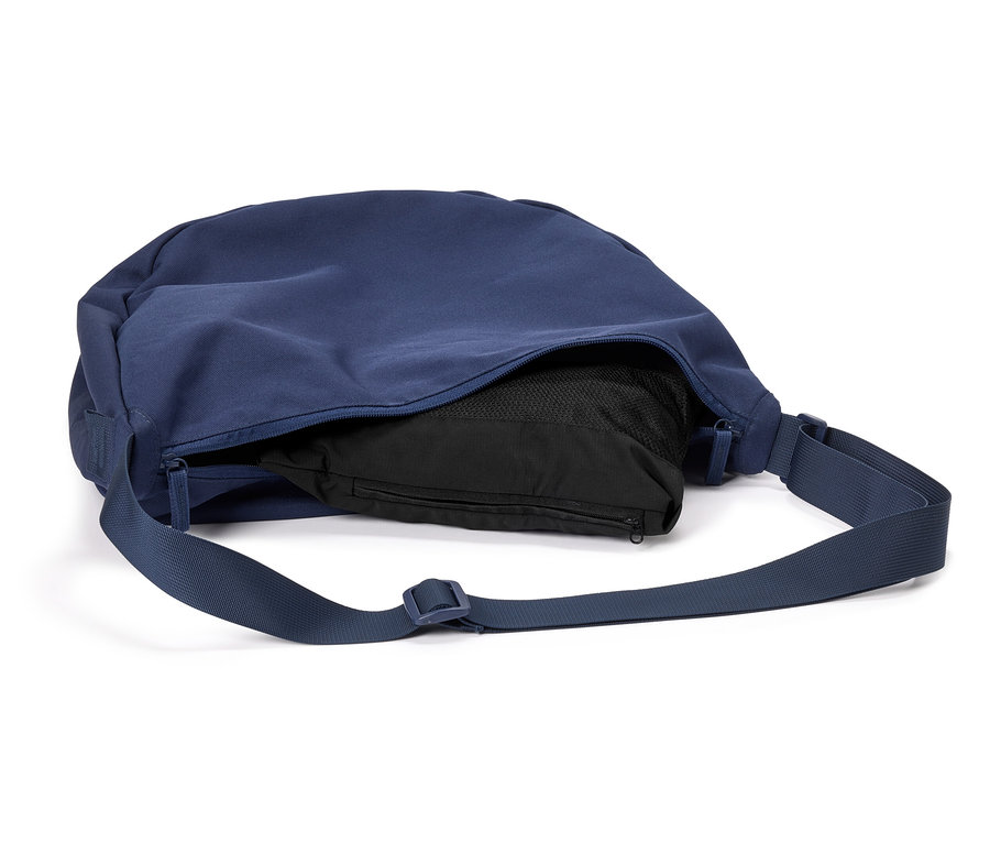 Marineblaue Umhängetasche mit schwarzem Inhalt und verstellbarem Träger liegt auf weißem Grund.