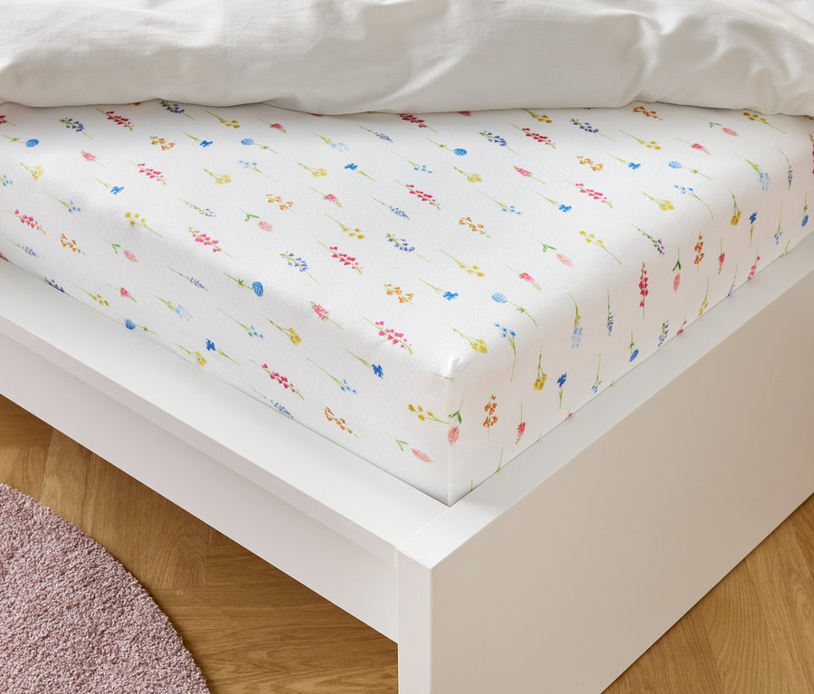 Ein weißes Spannbettlaken mit einem Blumenmuster liegt auf einem weißen Bettrahmen.