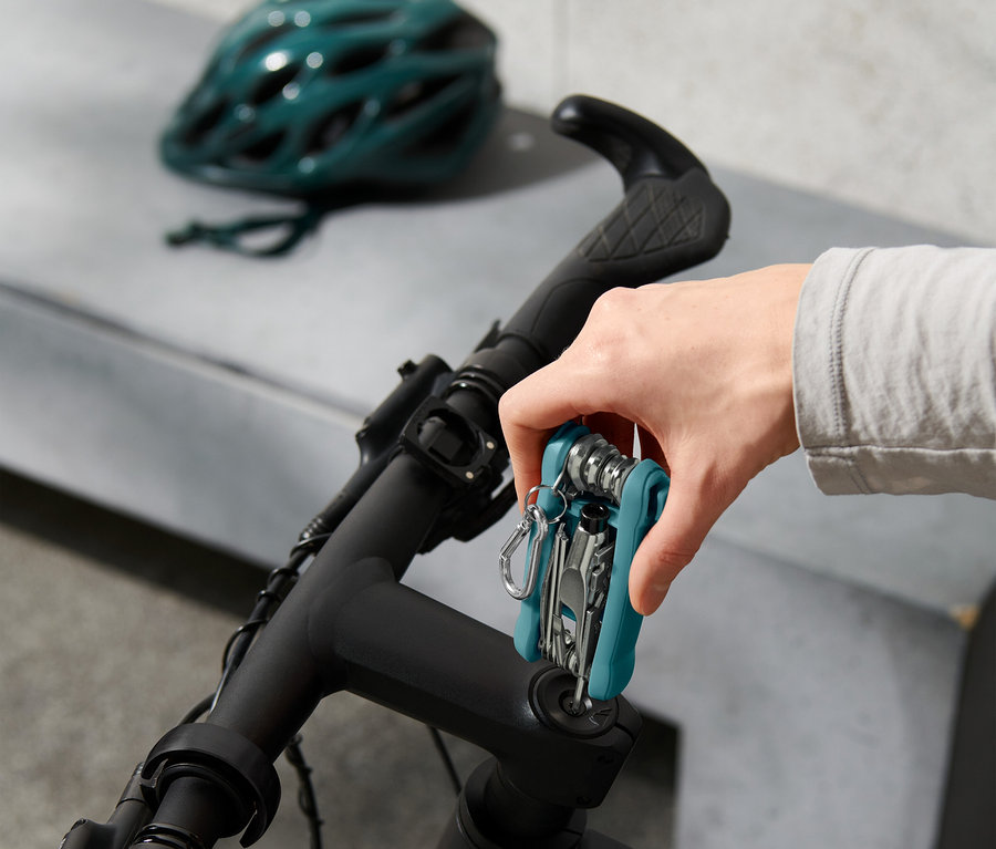 Hand befestigt Multifunktionswerkzeug am Fahrradlenker, im Hintergrund Fahrradhelm.