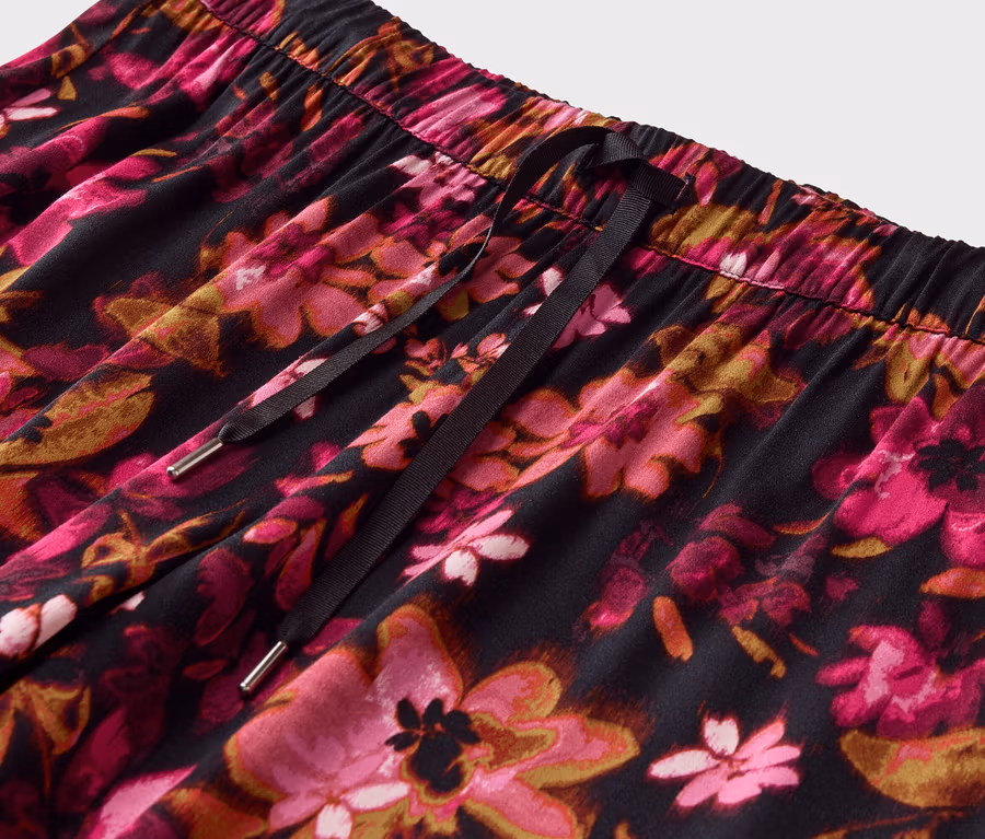 Nahaufnahme einer Hose mit Gummizug und Kordel, bedeckt mit einem pinkfarbenen Blumenmuster auf schwarzem Grund.