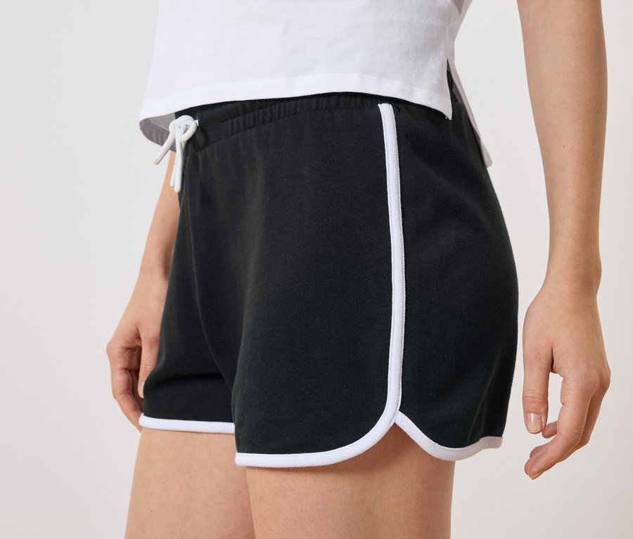 Nahaufnahme einer Frau, die schwarze Shorts mit weißen Seitenstreifen und weißem Kordelzug trägt.