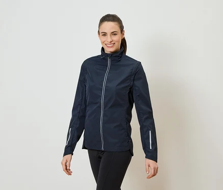 Eine Frau mit Pferdeschwanz trägt eine marineblaue Jacke mit durchgehendem Reißverschluss und schwarzen Leggings.