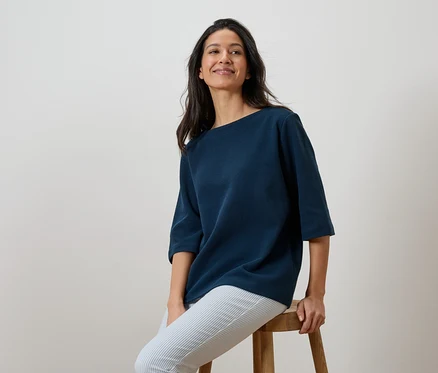 Frau sitzt auf einem Hocker und trägt ein marineblaues Shirt und gestreifte Hosen.
