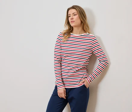 Frau mit gestreiftem Langarmshirt und blauer Jogginghose, eine Hand in der Hosentasche.