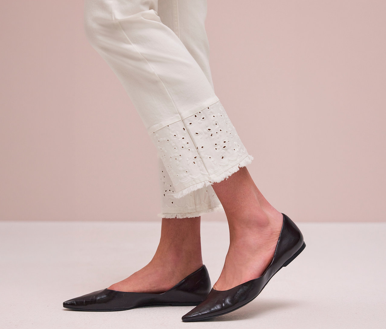 Person trägt weiße Street One Jeans mit besticktem, ausgefranstem Saum und schwarze spitze Ballerinas.