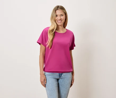 Eine Frau mit blonden Haaren trägt ein pinkes T-Shirt und blaue Jeans.