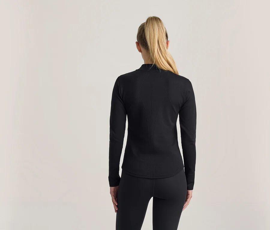 Frau von hinten, mit blonden Haaren im Pferdeschwanz, trägt ein schwarzes Langarmshirt und schwarze Leggings.