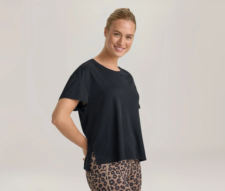 Lächelnde Frau mit Dutt, die ein schwarzes T-Shirt und Leggings mit Leopardenmuster trägt, Hände hinter dem Rücken.