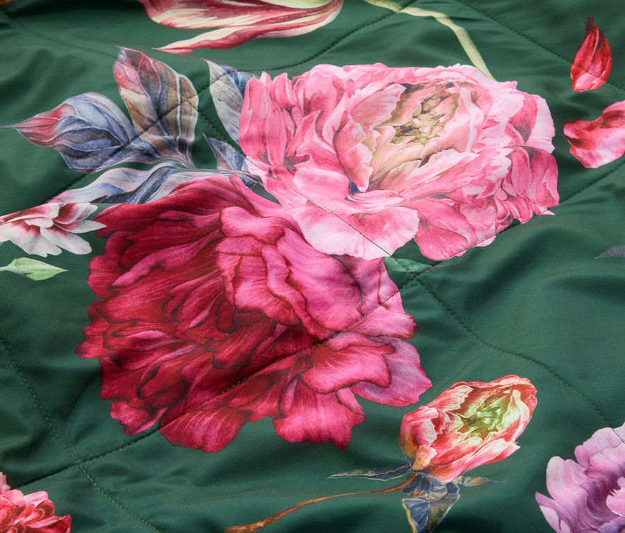 Nahaufnahme eines dunkelgrünen Steppstoffs mit großen rosa und roten Blumenmustern, darunter Pfingstrosen und Tulpen.