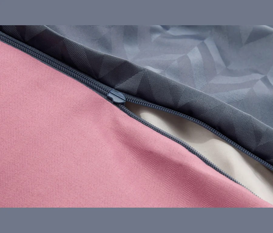Nahaufnahme eines dunkelblauen Reißverschlusses, der einen rosafarbenen Fischgrätstoff und einen graublauen Stoff mit geometrischem Muster verbindet. Der teilweise geöffnete Reißverschluss enthüllt einen hellen Stoff darunter.