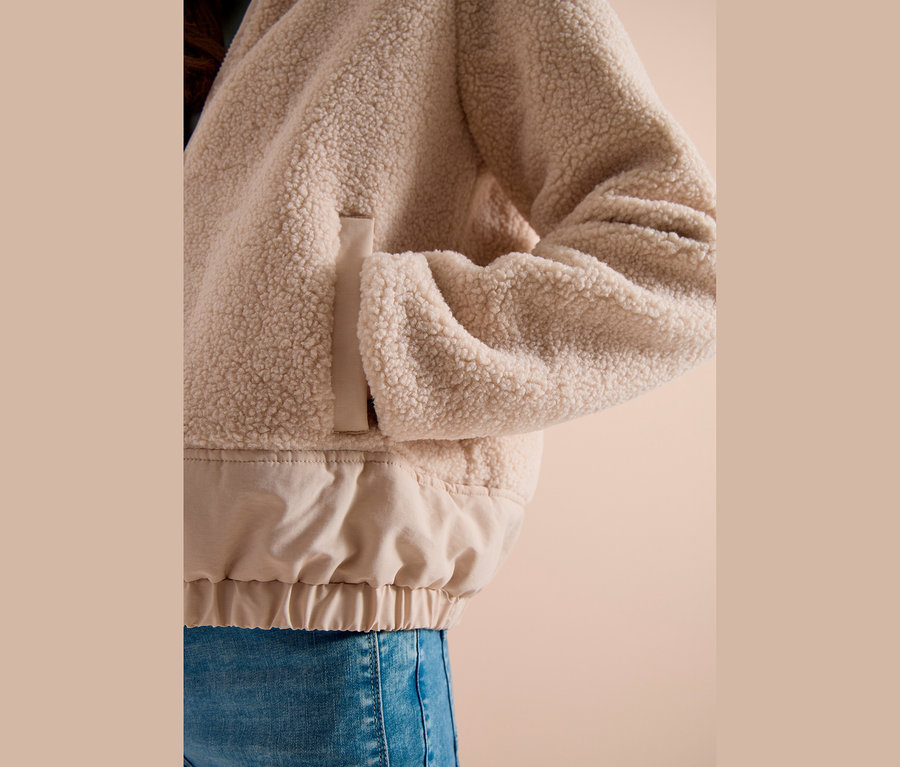 Person trägt beigefarbene, flauschige CECIL Jacke mit glattem, hellbeigem Gummizugsaum und blauen Jeans, Hand in der Tasche.
